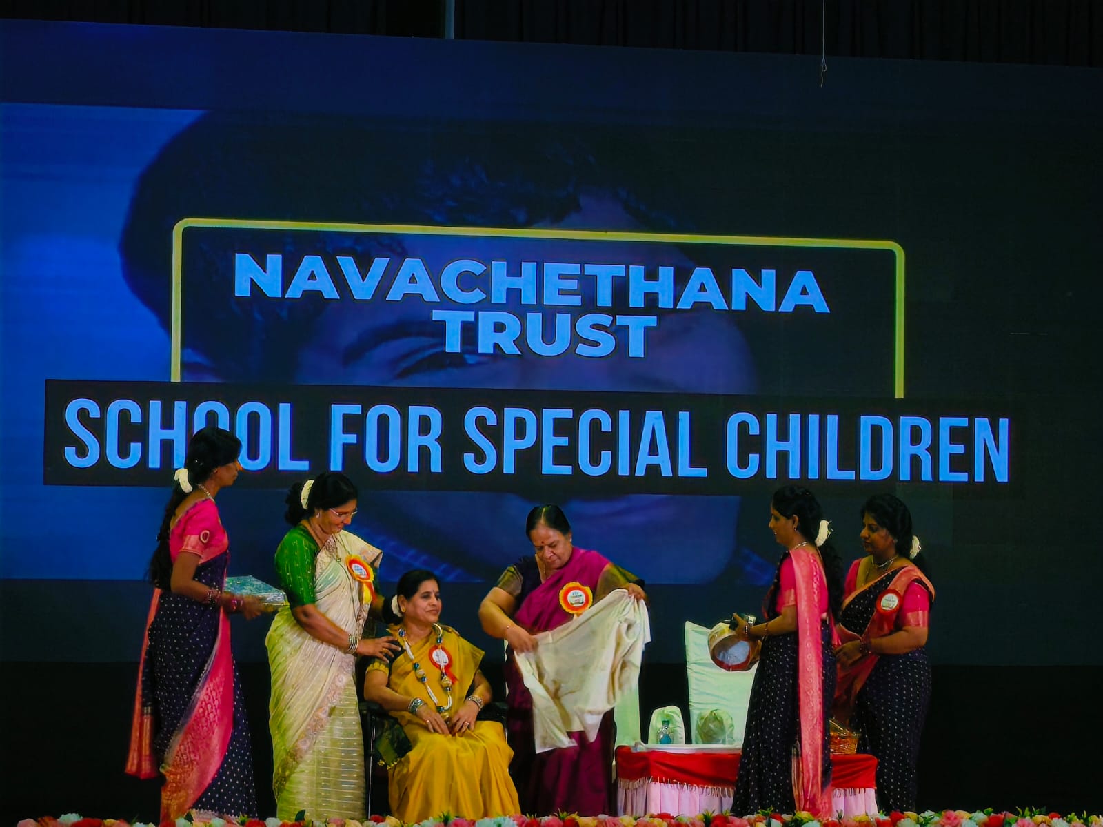 Staff members felicitated on stage beneath the Navachethana Trust School for Special Children title screen