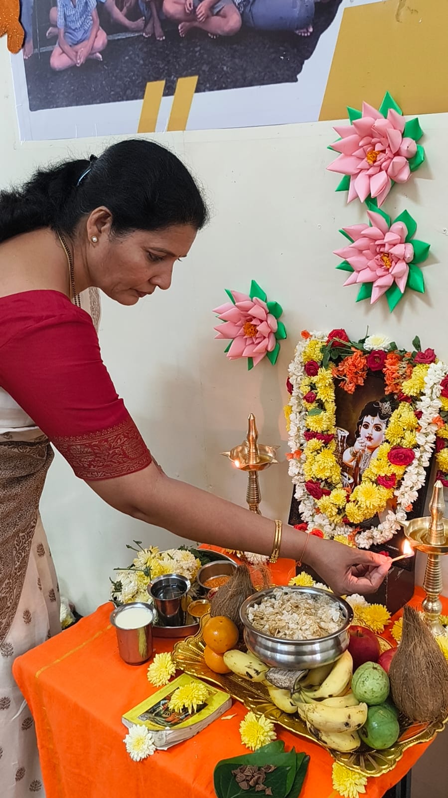 A staff member lighting a lamp and offering prayers at the Krishna Janmashtami altar
